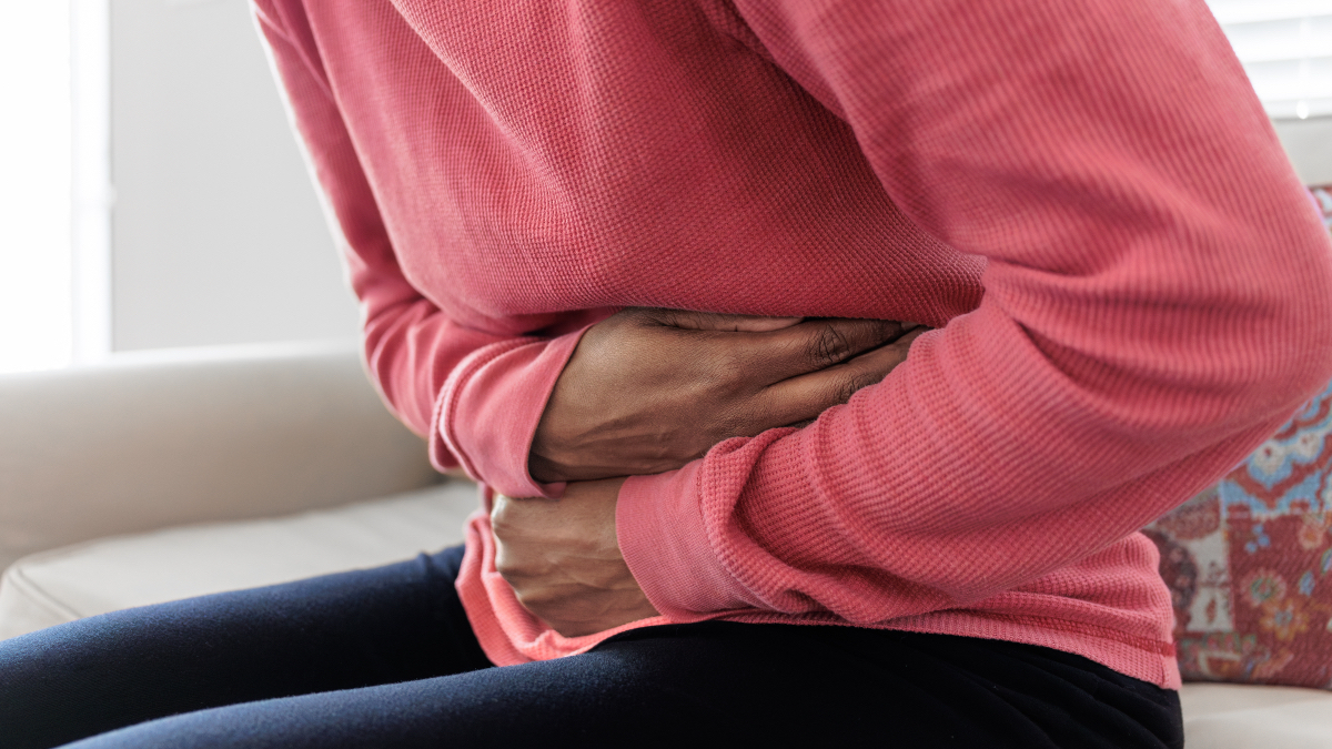 A woman in a pink sweater and black leggings clutching her stomach