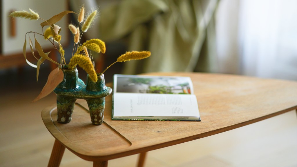 How to decorate a coffee table: Wooden mid-century modern coffee table decorated with an open hardcover book and bud vase of dried flowers