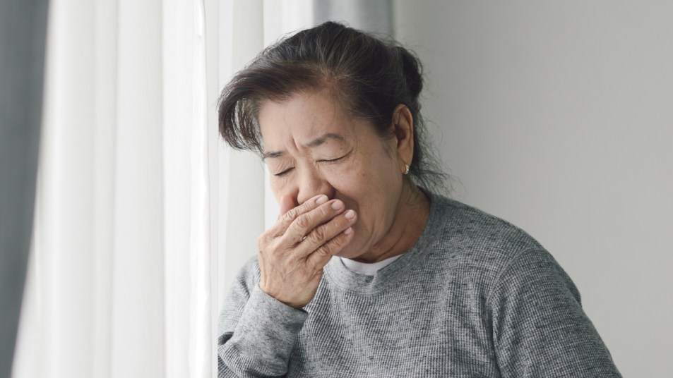 mature woman coughing at home by a curtain - sign of air pollutants