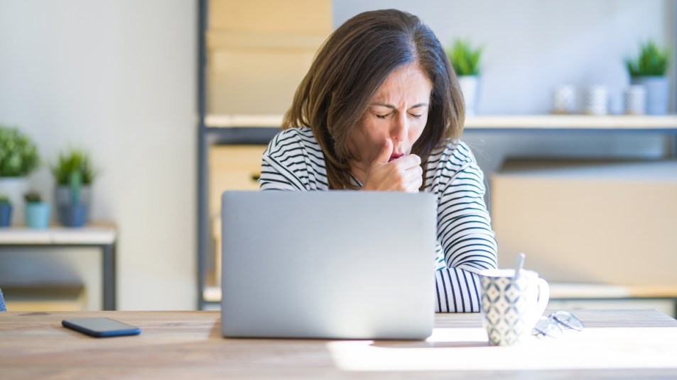 Woman coughing while working at laptop