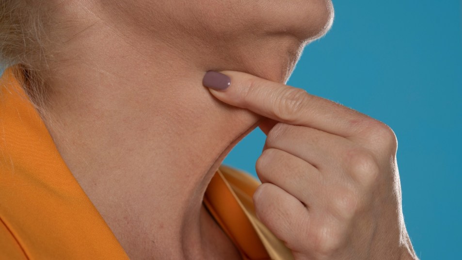 A close-up and side profile view of a caucasian senior lady pinching the loose skin at the front of her throat. Commonly called a turkey neck and corrected with a platysmaplasty