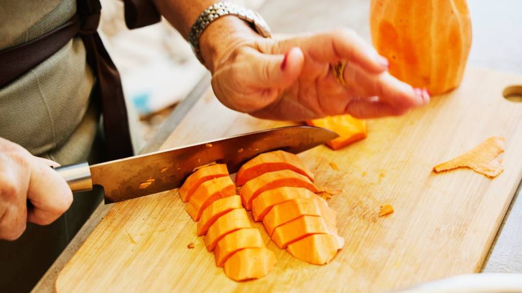 healthy aging tips: Close up shot of mature woman chopping sweet potatoes on cutting board while taking vegetarian cooking class