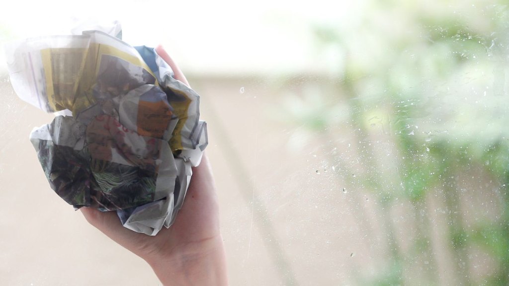 Woman using old newspaper to clean the glass.