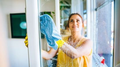 How to Clean Windows Without Streaks:Beautiful smiling young woman cleaning and wiping window with spray bottle and rag stock photo - stock photo