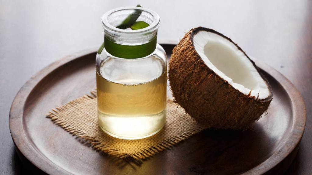 Coconut oil with fresh coconut half on wooden background, which can help for folks who want to know how to stop bleeding gums