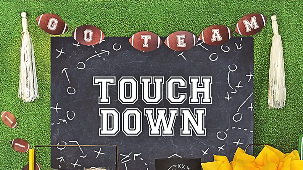 DIY football decorations: Turf and play call backdrop made by taping a grass-printed tablecloth and festive "touchdown" poster board to wall, then decorating with a football tassel banner