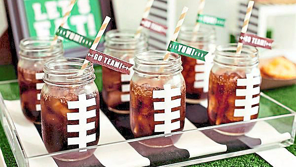 DIY football decorations: Football-inspired soda drink jars made by taping duct tape "laces" to outside of Mason jars, then filling each with cola and a pennant-kissed straw
