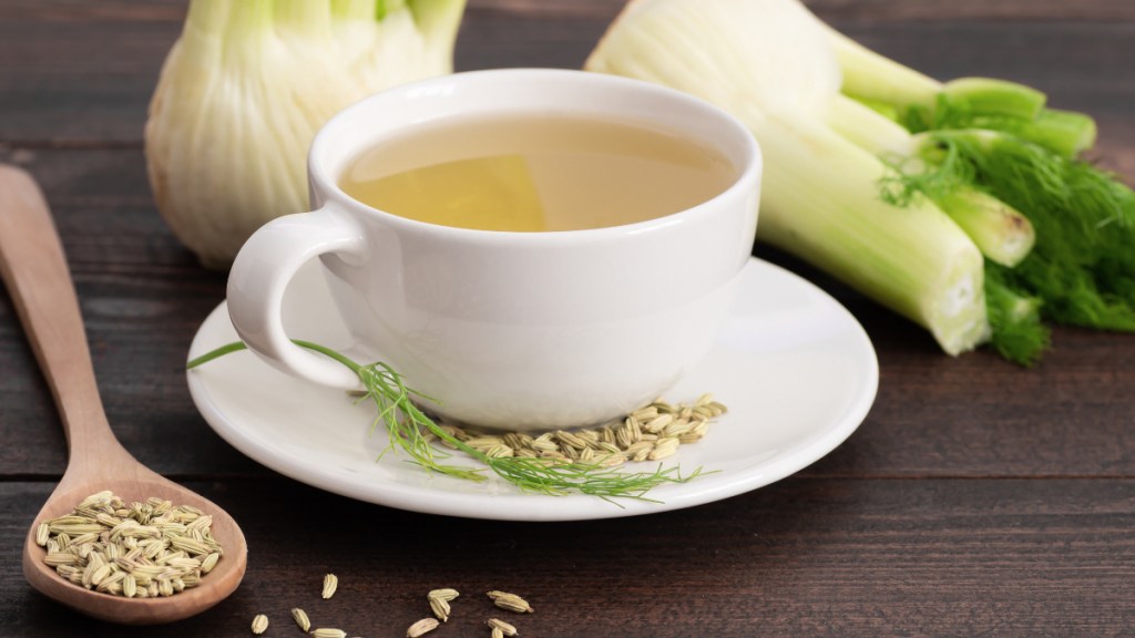 A white mug with fennel tea for bloating beside fennel seeds and fresh fennel