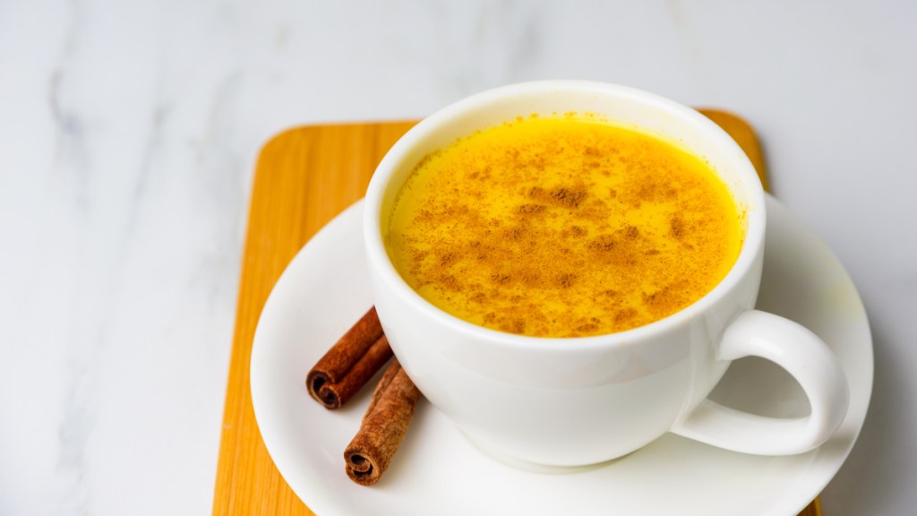 A cup of golden milk, made with turmeric, in a white cup on a wooden tray