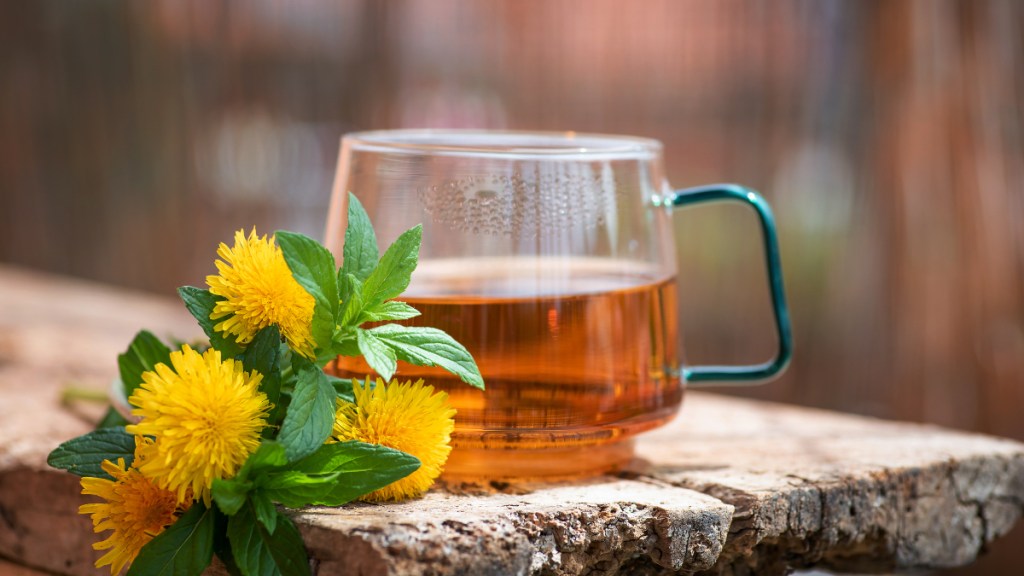 A cup of dandelion tea for bloating next to fresh dandelion flowers on a wooden table