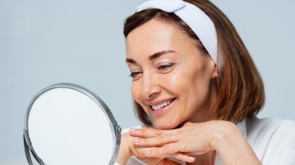 Mature woman smiling looking in makeup mirror at tinted eyebrows