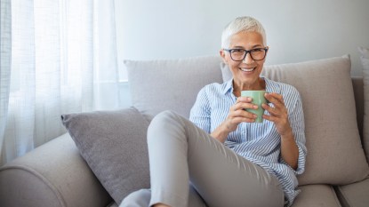 A woman with grey hair wearing a striped shirt holding a cup of tea as part of an arthritis self-care strategy