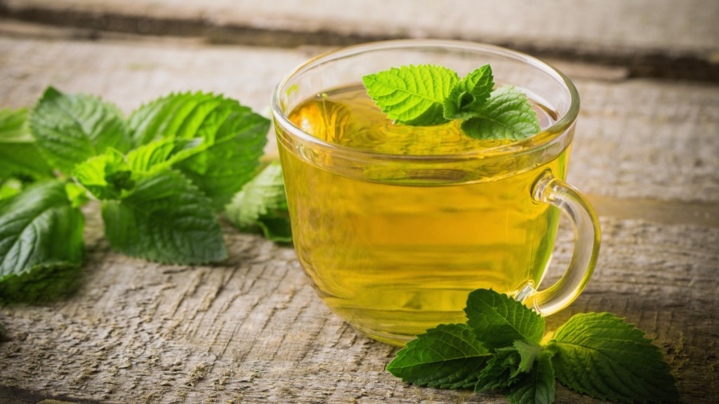 A cup of peppermint tea for bloating on a wooden table with fresh mint leaves