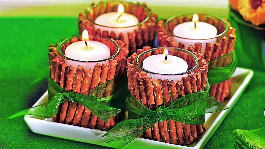 DIY football decorations: Pretzel candle twinklers made by covering outside of a glass votive candle cup with pretzel sticks, then wrapping with green ribbon and displaying 4 on a square tray