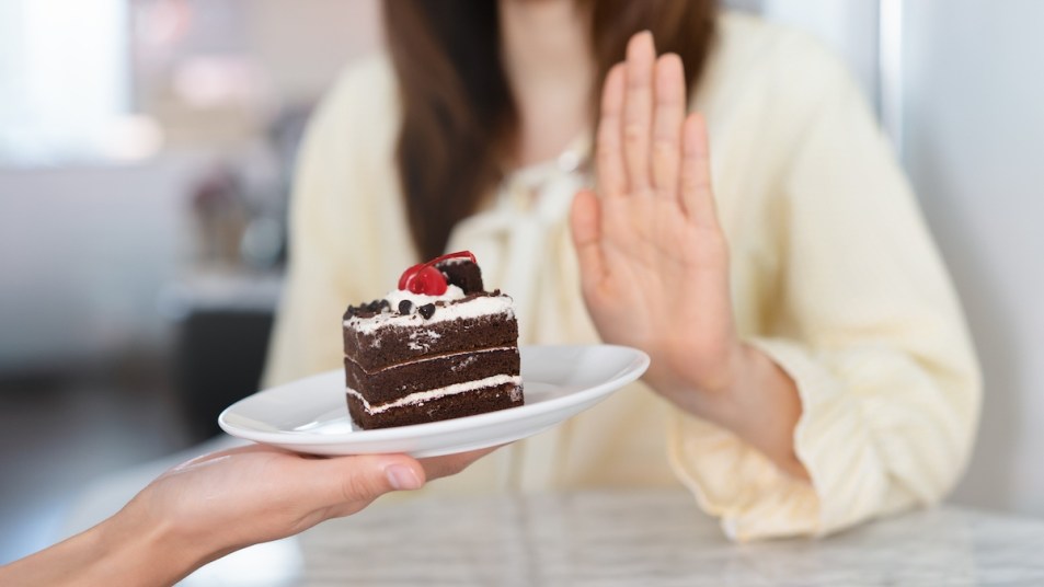 Woman holding up hand to refuse piece of chocolate cake