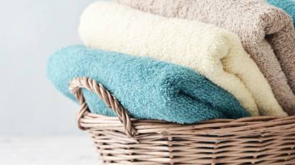 How to fold towels to save space: Bath towels of different colors in wicker basket on light background