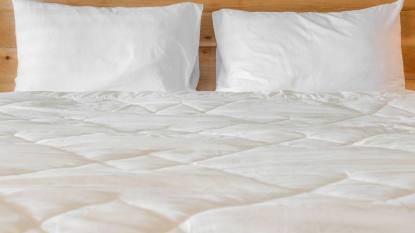 How to Wash a Down Comforter: White pillows on empty bed in bedroom.