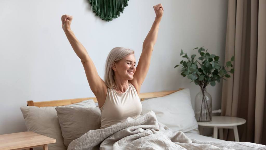 spring equinox 2024: Active happy mature female wake up from good healthy sleep stretching sitting in bed at home, smiling positive senior woman awaken in comfortable bedroom feel optimistic welcome new day