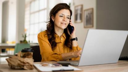 Work from home human resources jobs: Smiling businesswoman using laptop while talking on mobile phone at desk in home office