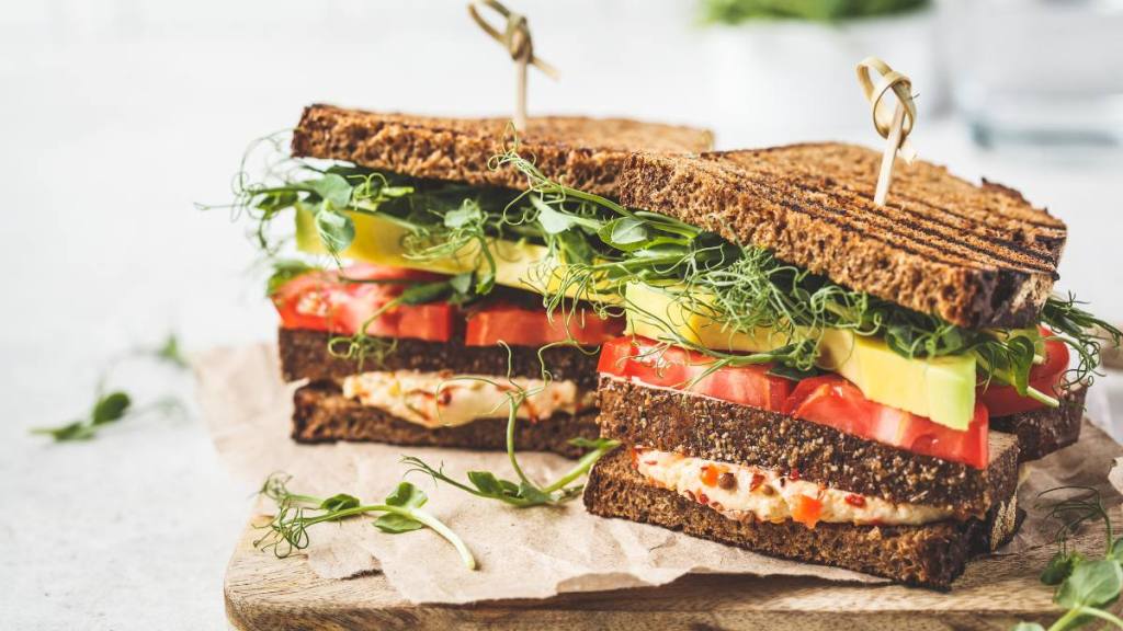 Plant Based Diet For Weight Loss: Vegan sandwich with tofu, hummus, avocado, tomato and sprouts on board.