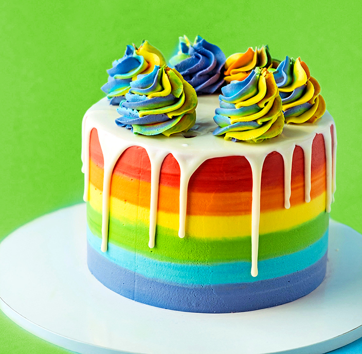 Rainbow cake with whipped cream top on the blue background. Birt