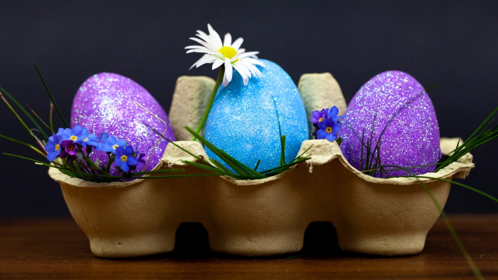 Cool Easter egg designs: Three purple and blue Easter eggs decorated with glitter and displayed in an egg carton