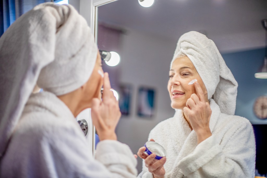 mature woman applying face moisturizer