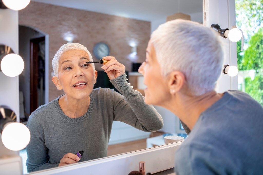 mature woman putting on mascara in mirror