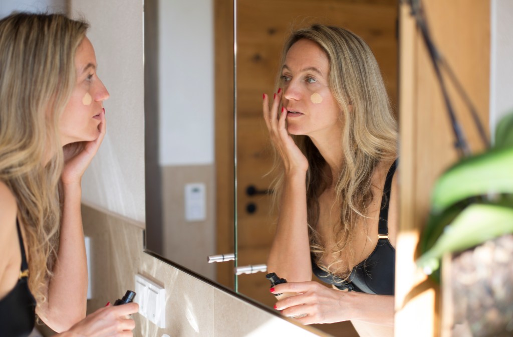 mature woman applying tinted sunscreen in mirror