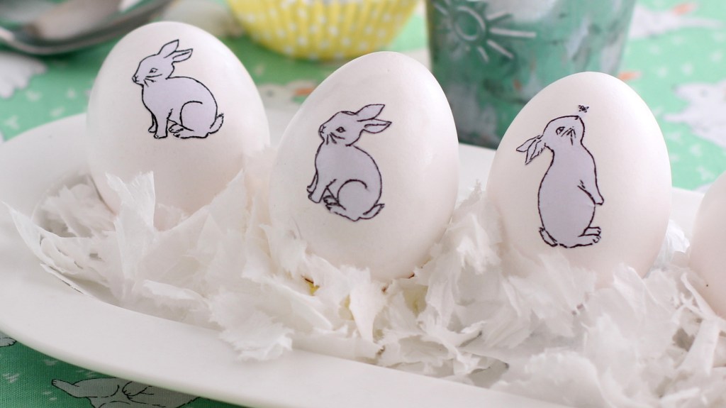 Cool Easter egg designs: Plain un-dyed Easter eggs decorated with bunny temporary tattoos and displayed on a feather-filled tray