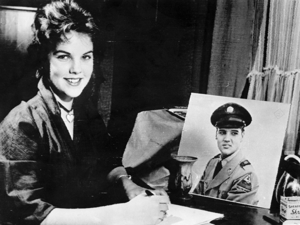 Priscilla Beaulieu poses with a portrait of Elvis Presley while writing him a letter, 1960