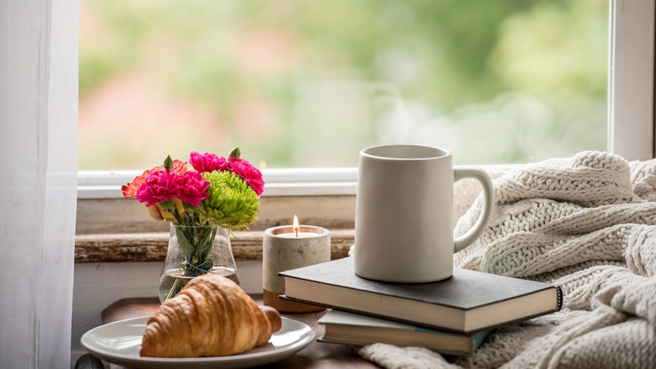 Best cozy mysteries: book by window with coffee, blanket and fresh flowers