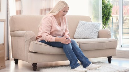 Woman sitting on couch and holding her knee in pain