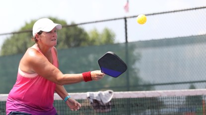 a senior woman hits a ball competing in a senior pickleball tournament