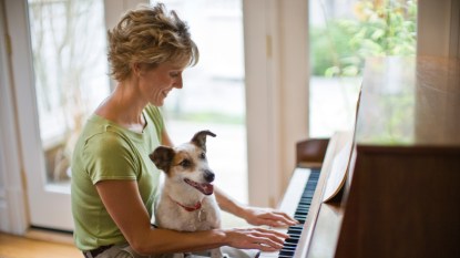Smiling mid-adult woman playing a piano with her pet dog on her lap.