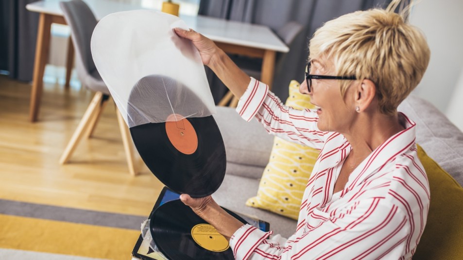 older woman with short blonde hair in a collared shirt looking at vinyl record happily remembering past with nostalgia