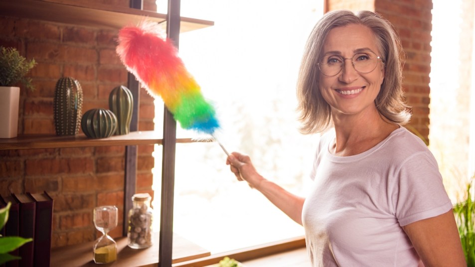 Woman posing with rainbow duster as she cleans shelf