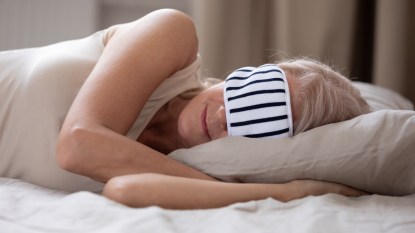Woan sleeping in bed wearing striped eye mask