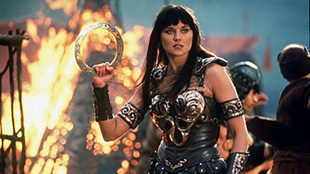 Woman in warrior costume, fire behind her; Lucy lawless