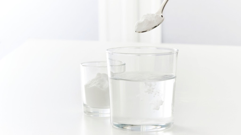 A glass of water with a spoonful of baking soda being added to it