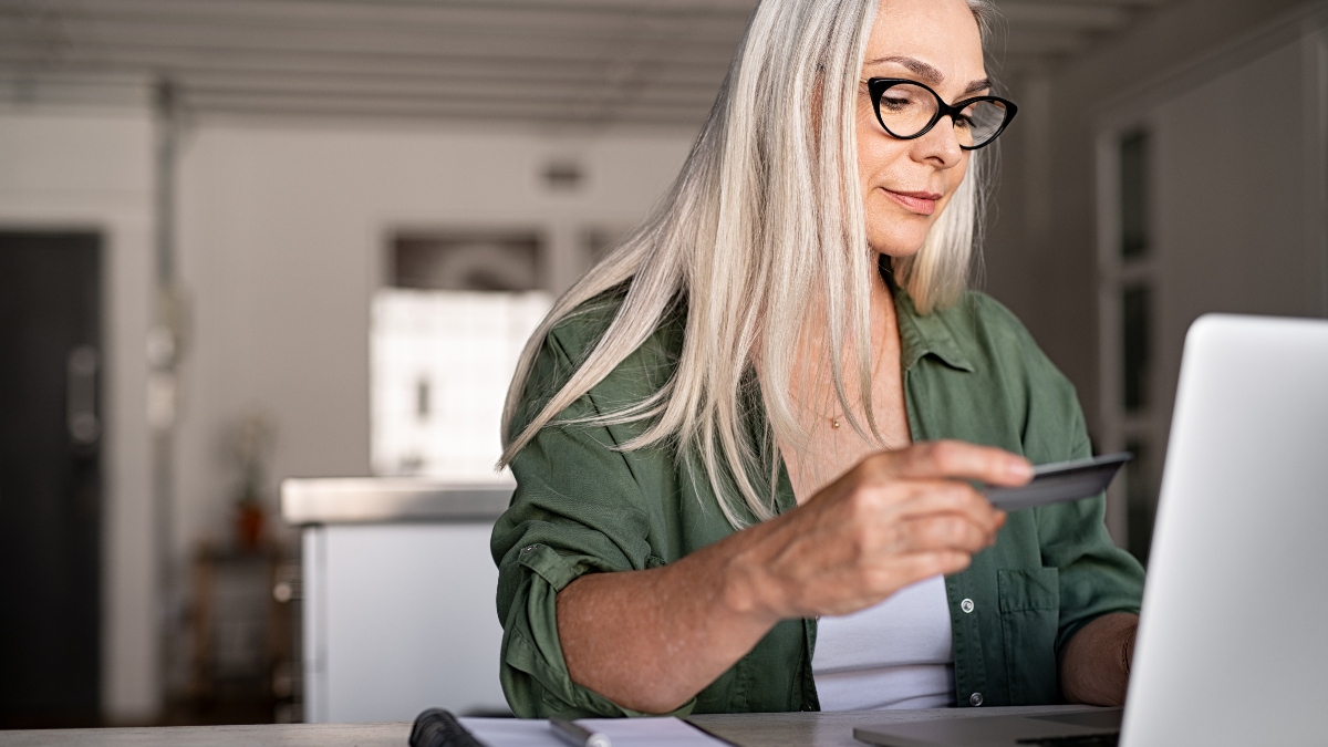 Mature woman using credit card making online payment at home. Successful old woman doing online shopping using laptop. Closeup of retired fashionable lady holding debit card for internet banking account.