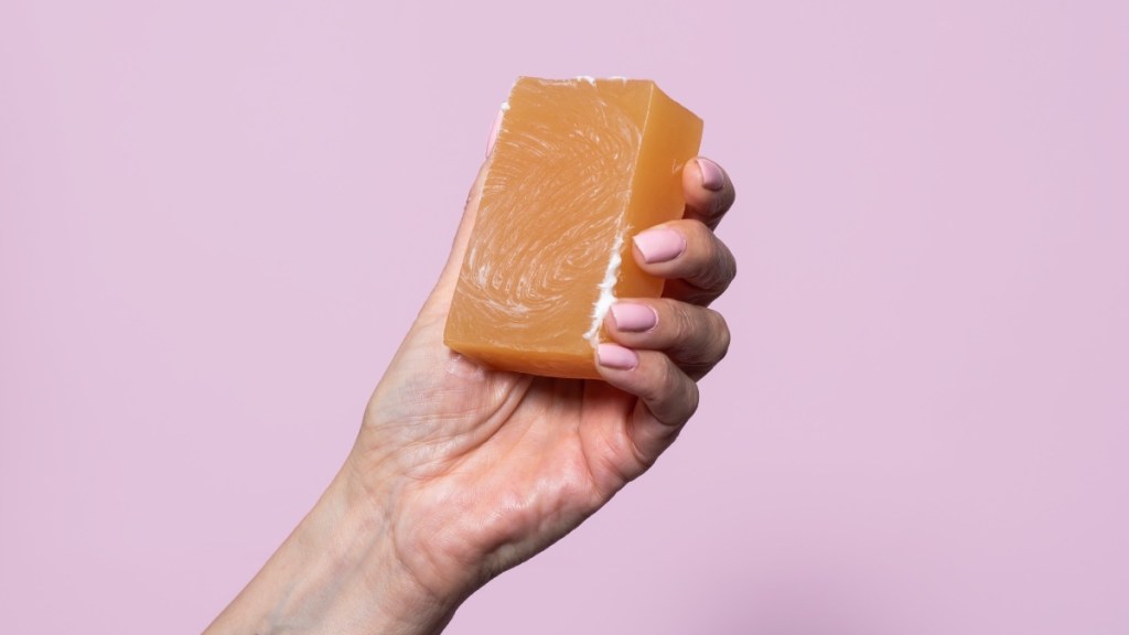 A woman's hand holding a natural bar of soap against a lilac background