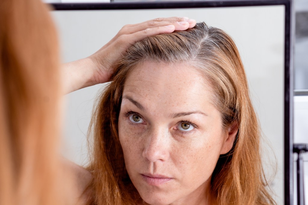 mature woman looking at gray roots in hair in mirror