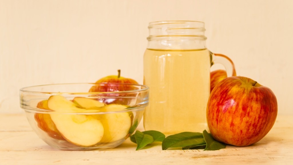 A glass of apple cider vinegar beside fresh apples