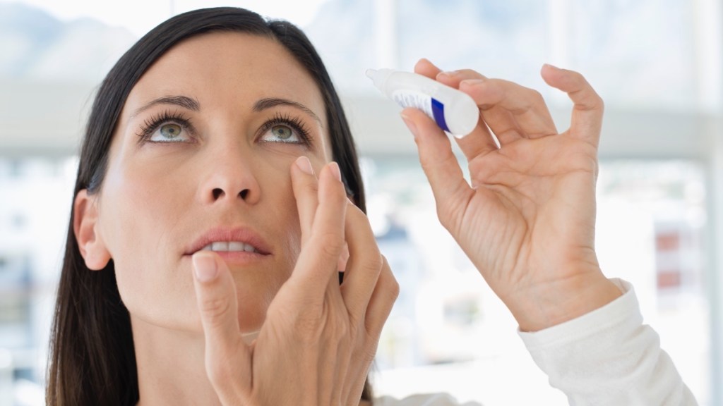 A woman with dark hair looking up while applying eye drops