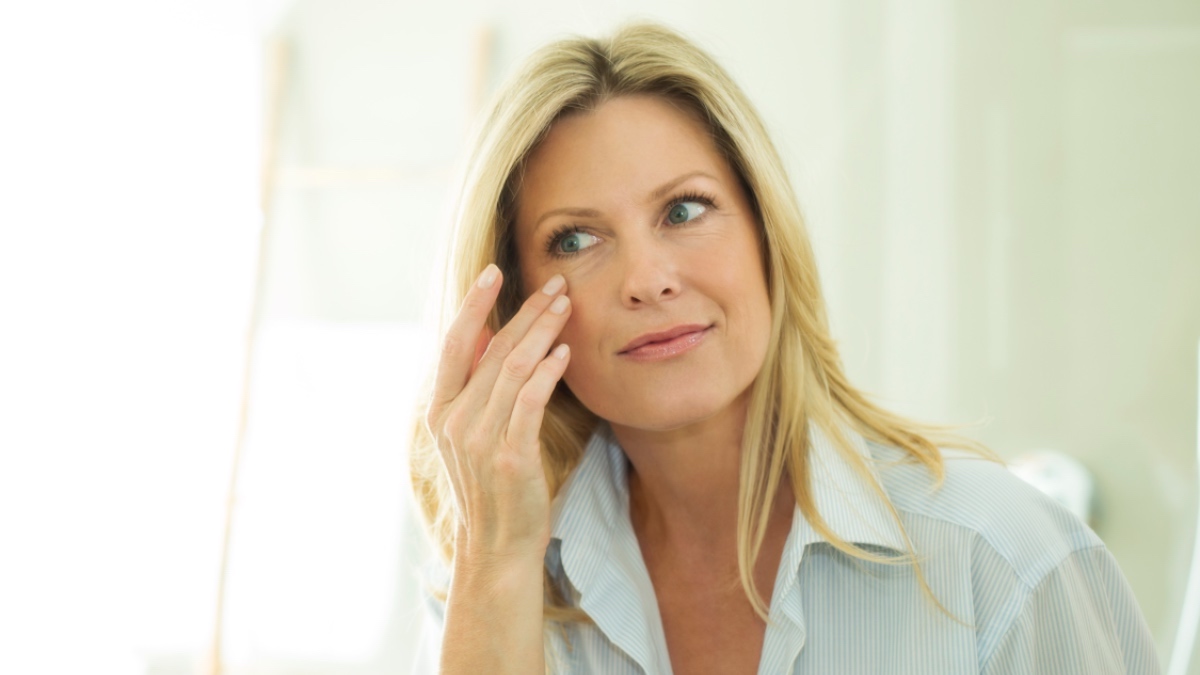 A blonde woman touching her face while looking the mirror wondering what is the fastest way to heal a swollen eyelid
