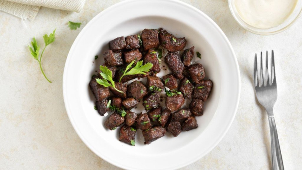 air fryer steak bites in white bowl with herbs