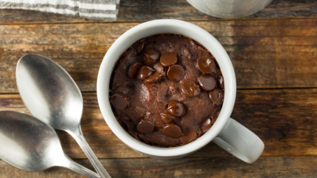 microwave brownie in white mug with chocolate chips with spoons on the side