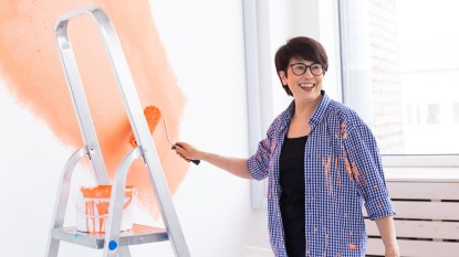 Woman painting white wall with orange paint