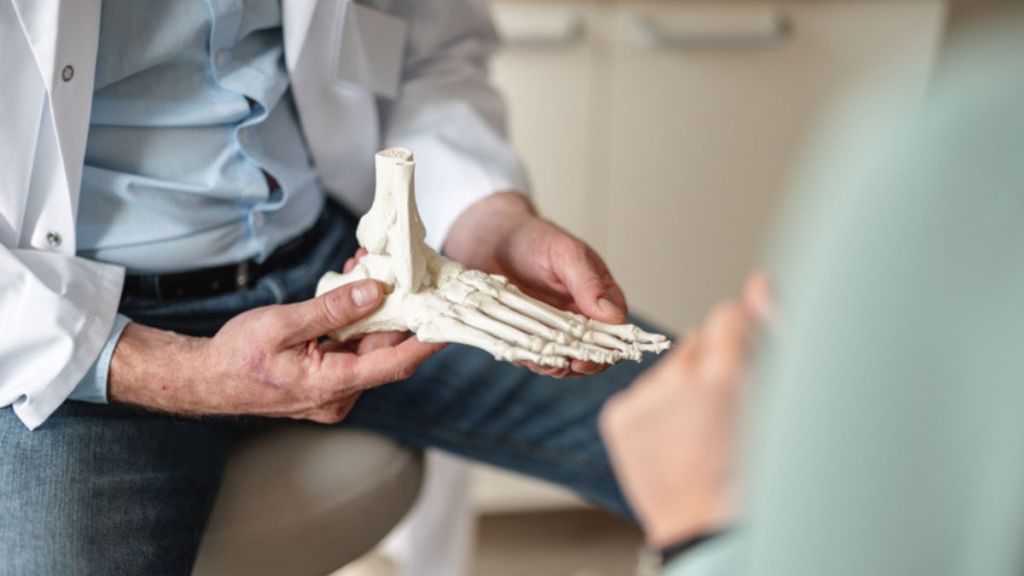 doctor showing bones of a foot skeleton to patient before foot surgery to remove a tailor's bunion